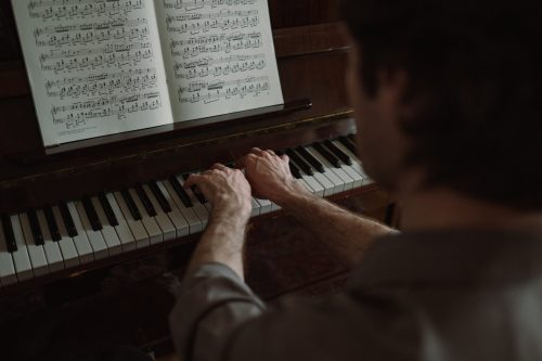 Mężczyzna gra utwór na pianinie. Na pianinie umieszczone są nuty.